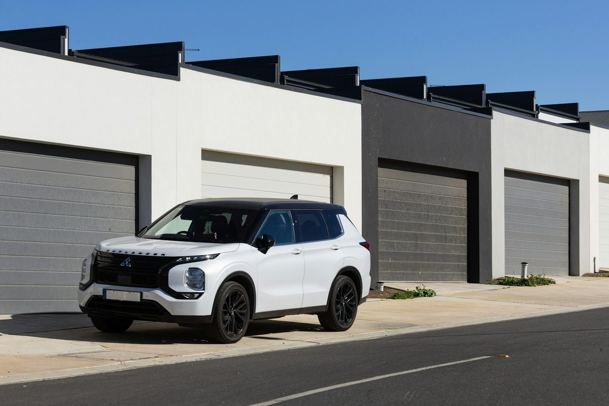 Hvit SUV parkert foran en moderne garasjerekke i solskinn